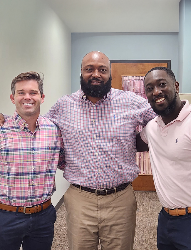 3 smiling employees standing together in an office.